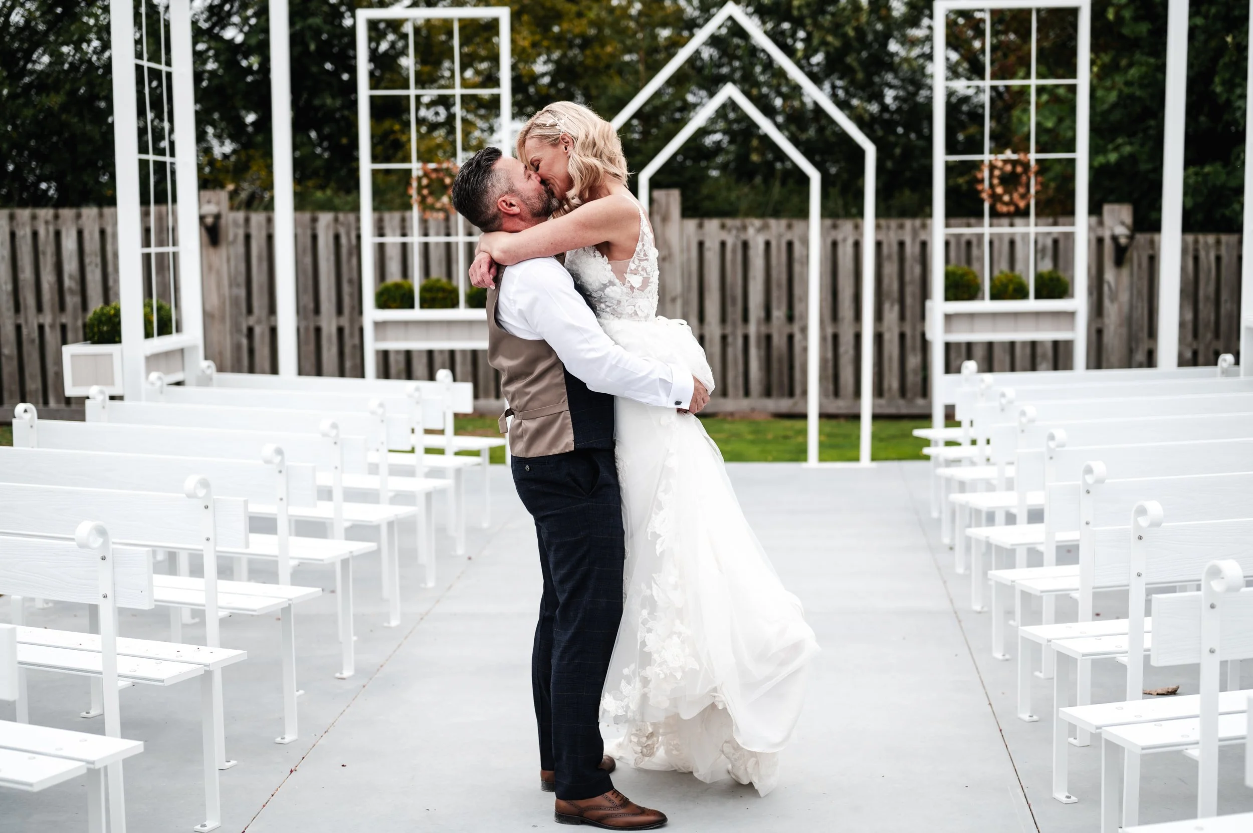 Cheshire Wedding Photographer - Bride and groom in wedding attire kissing in the middle of the aisle of outdoor wedding