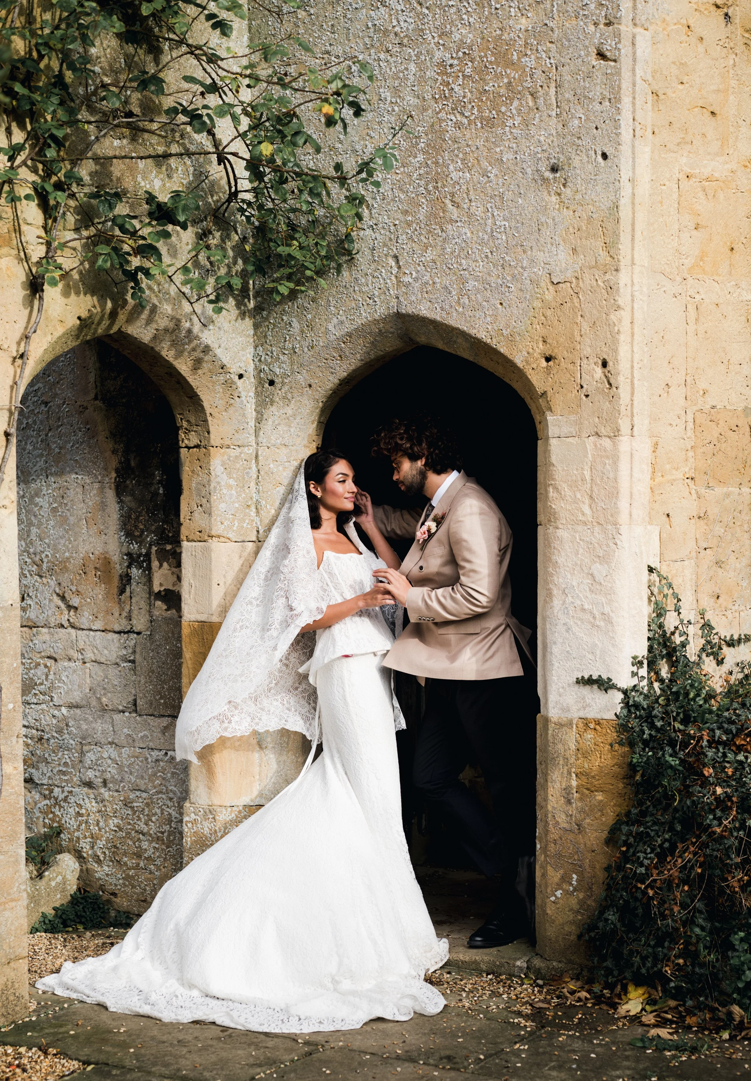 A bride and groom sharing a romantic moment outside a stone archway, with greenery around them at sudeley castle, Gareth roy photography