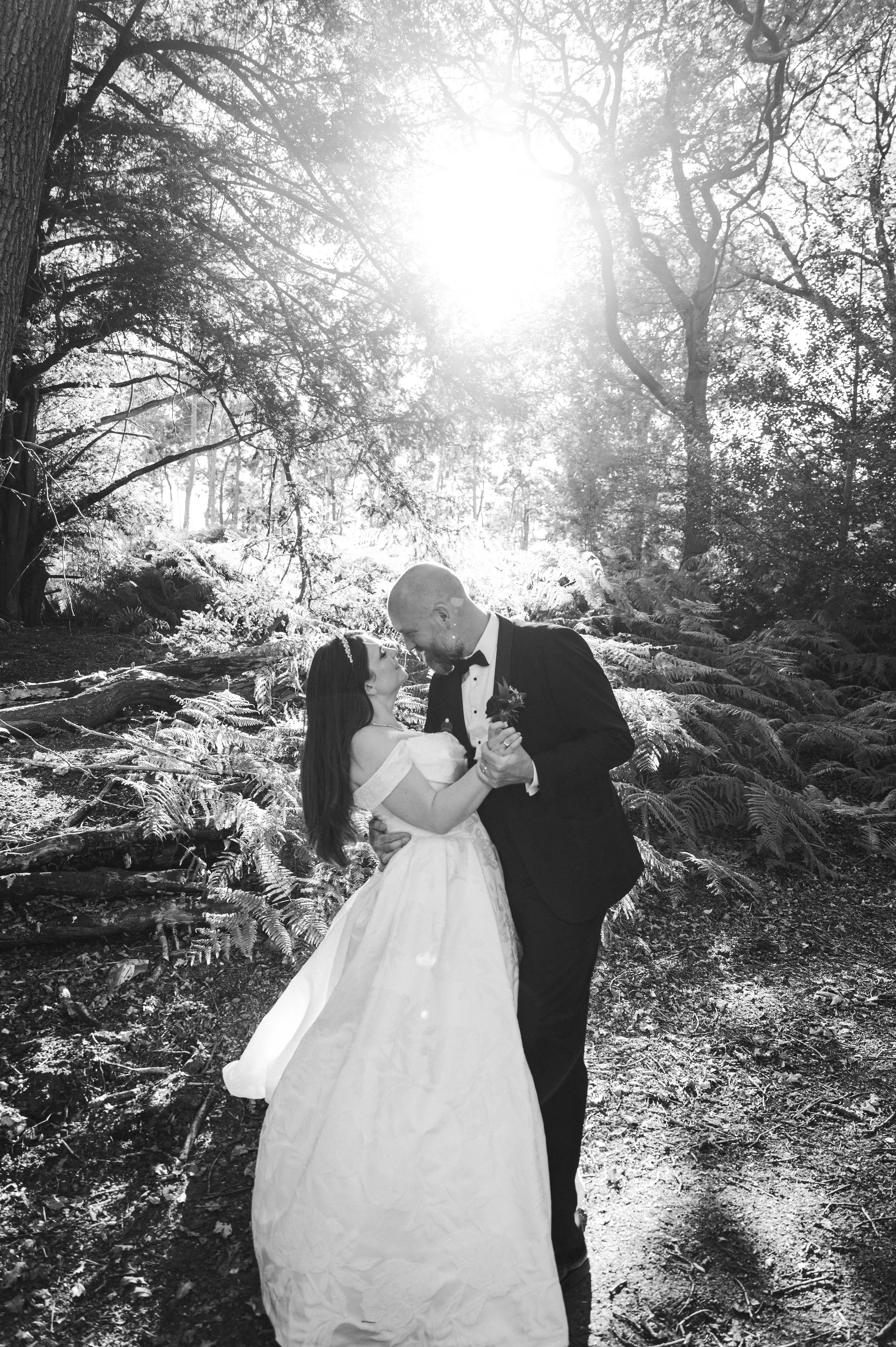 Peckforton Castle - black and white image of bride and groom in wedding attire in an embrace, standing in woodland