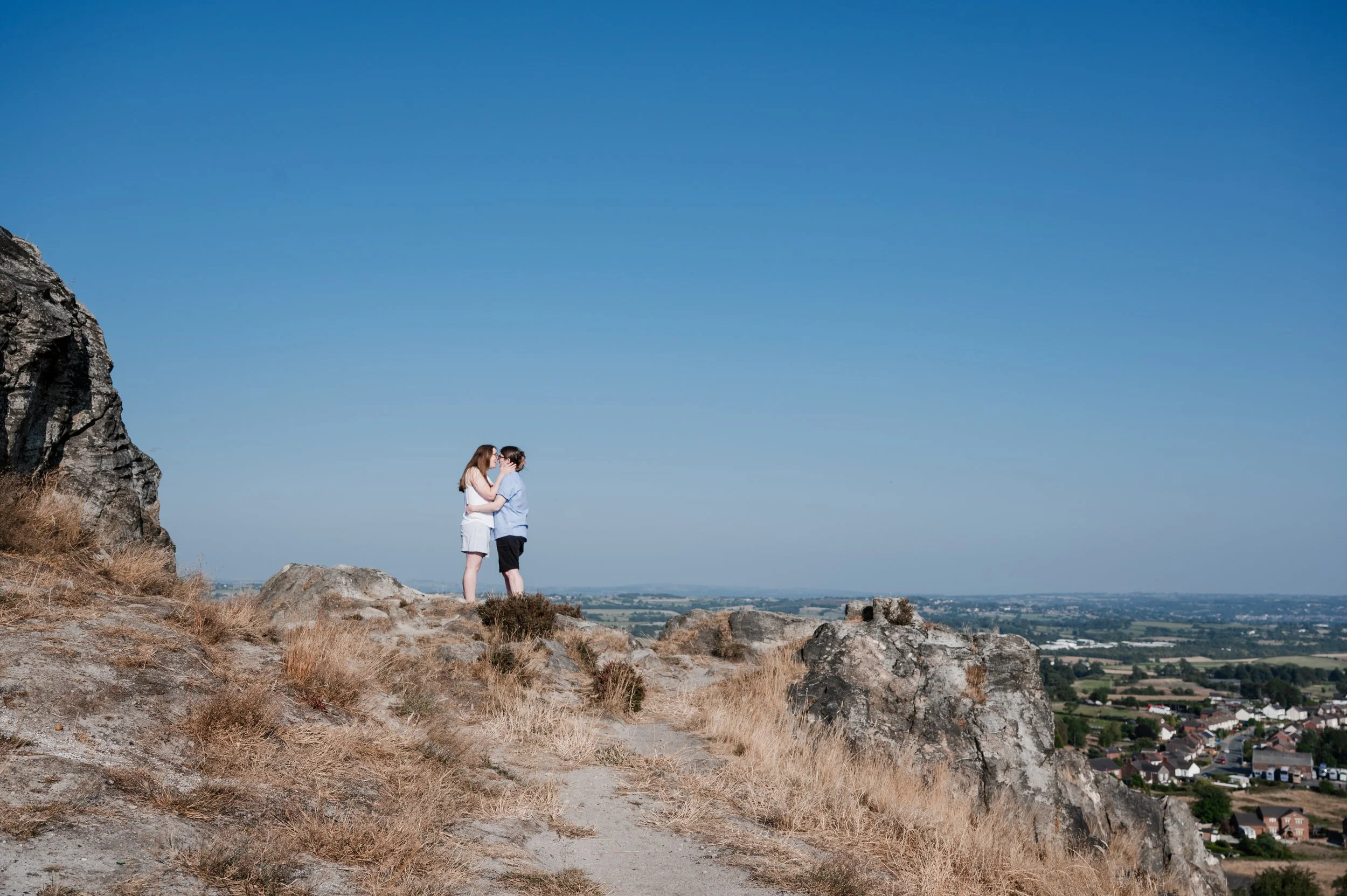 Mow Cop Engagement Shoot - two women stood in front of a landscape of Cheshire while embracing and kissing