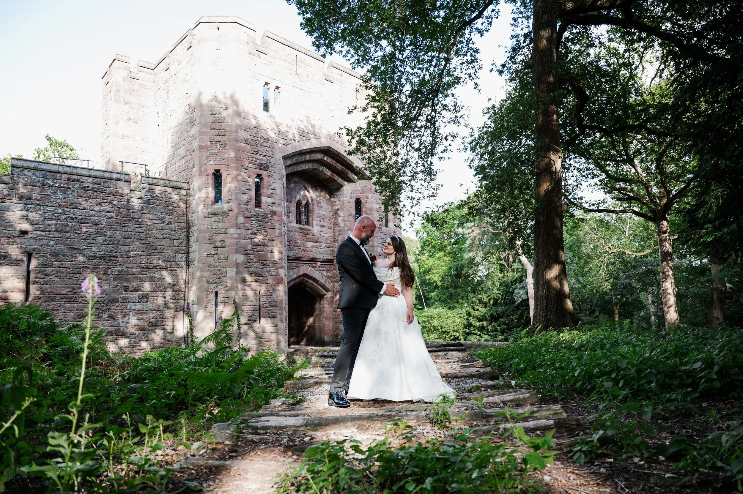 Peckforton Castle - bride and groom in wedding attire standing in embrace in front of Peckforton Castle