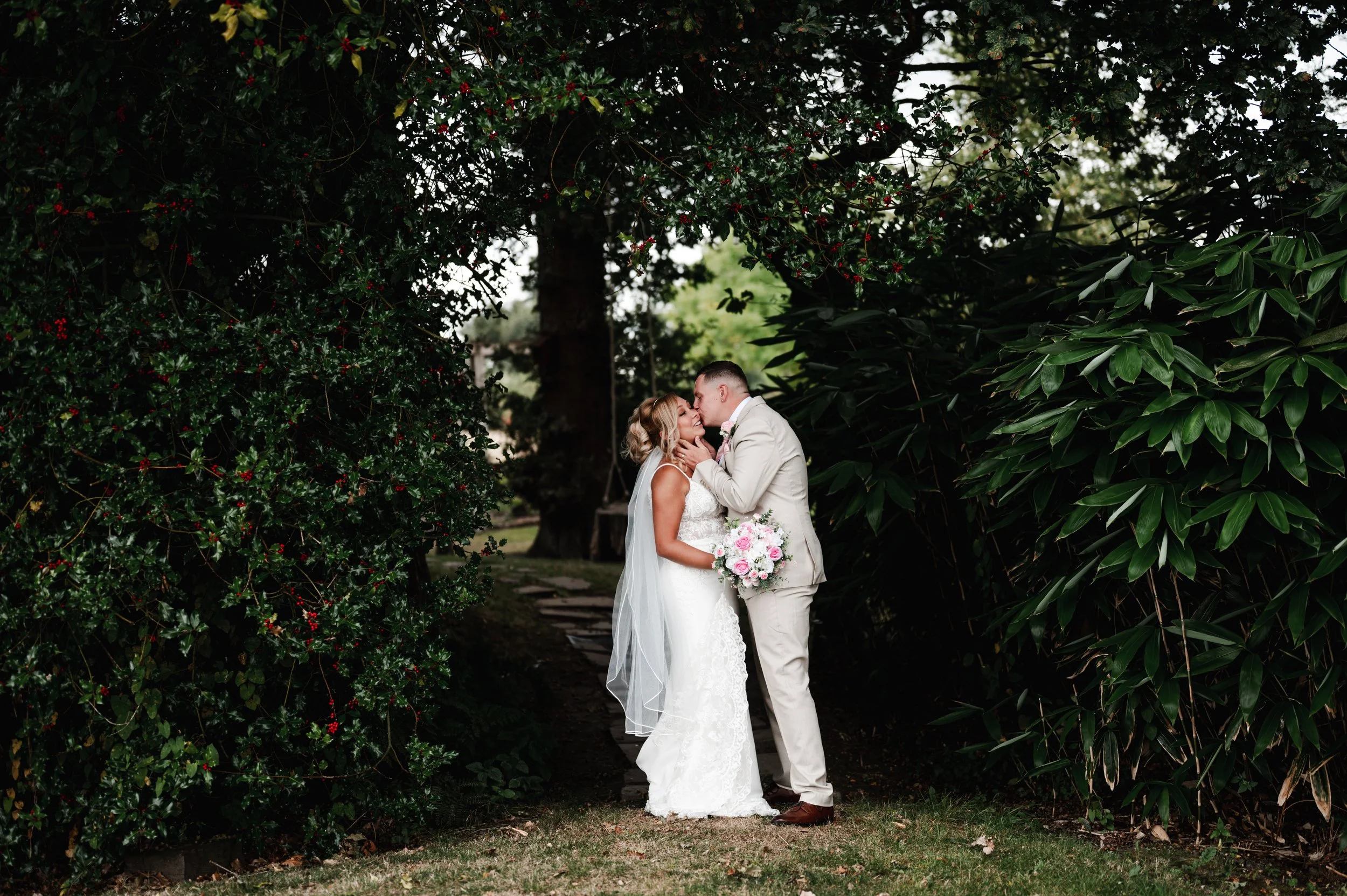 The Love Shack - groom and bride in wedding attire, kissing in front of forest foliage