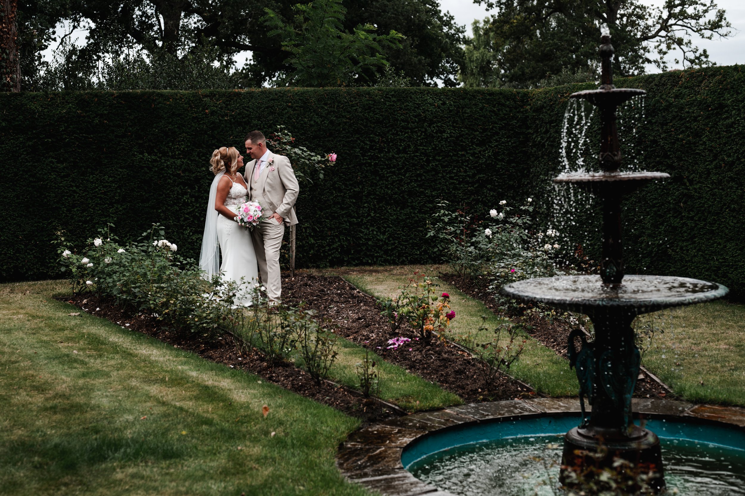 The Love Shack - Groom and bride in wedding attire, looking at each other in front of a fountain in gardens 