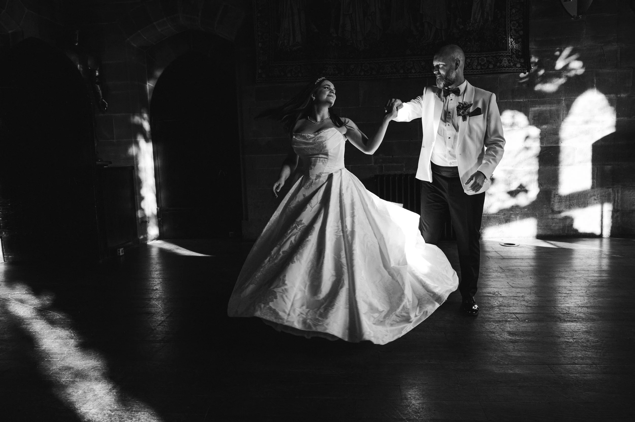 Peckforton Castle - Black and white image of bride and groom in wedding attire dancing in castle hall. 