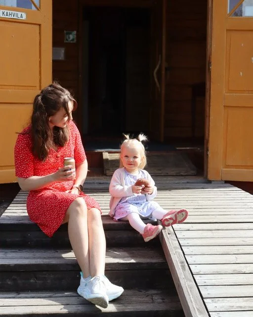 A young woman and a little girl sitting on a wooden porch outside a cabin, each holding a jar.