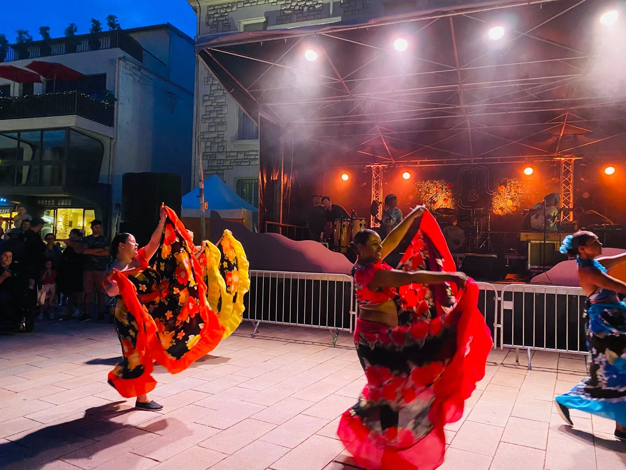 Danseurs déguisés en fleurs colorées dans une performance en plein air, avec un fond de scène illuminée.