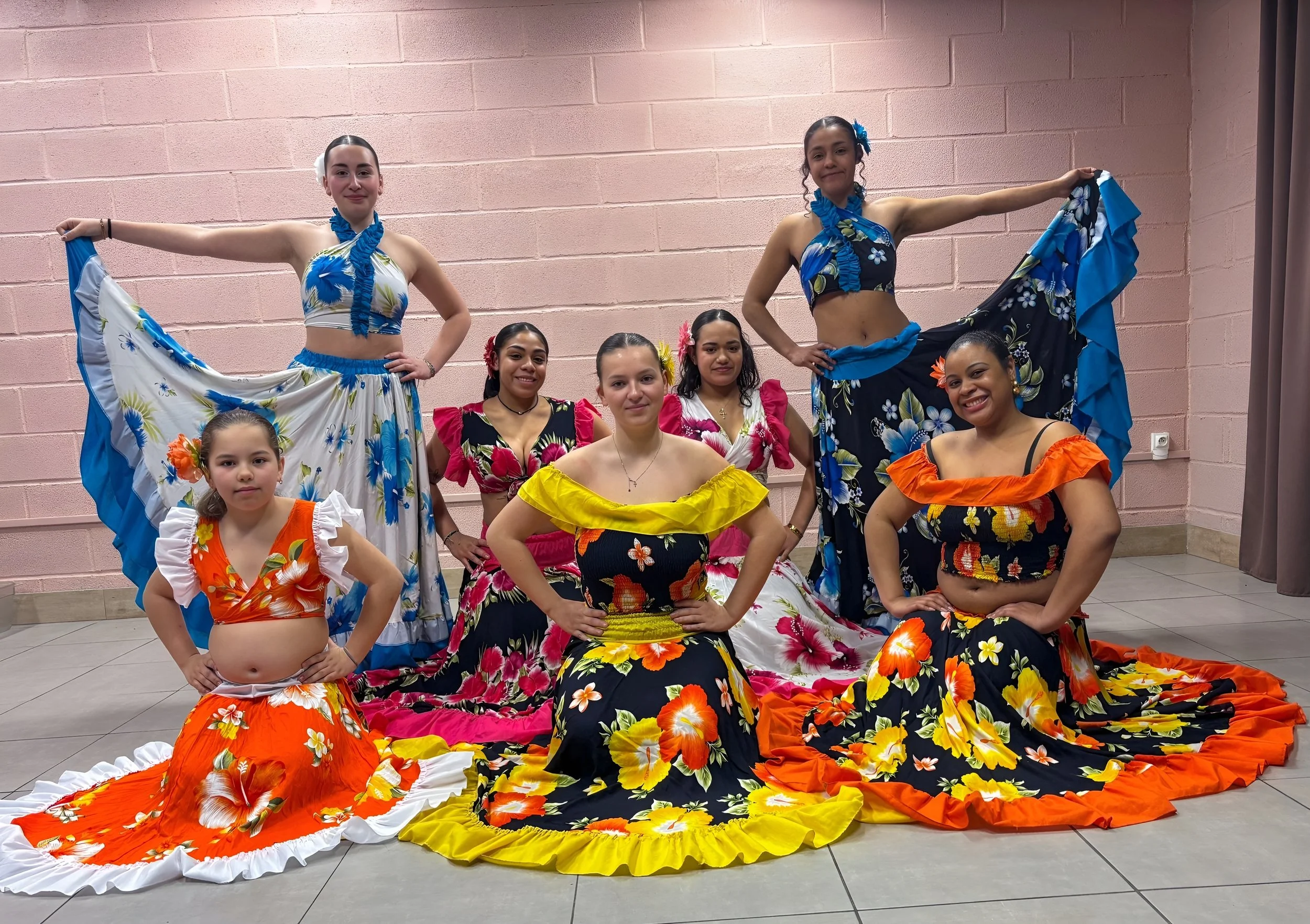 Groupe de jeunes femmes en tenues de danse en floral coloré, posant devant un mur rose.