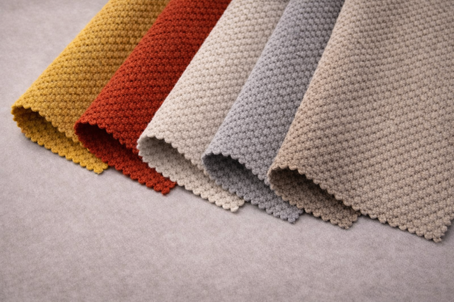 Seis muestras de tela en colores beige, gris, blanco, rojo, amarillo y marrón, con textura de tela acartonada, colocadas en línea sobre un fondo gris.