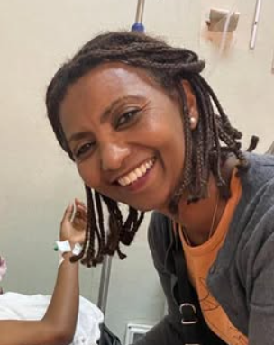 En kvinna med korta, vågiga dreadlocks som ler, troligtvis i ett sjukhusmiljö
