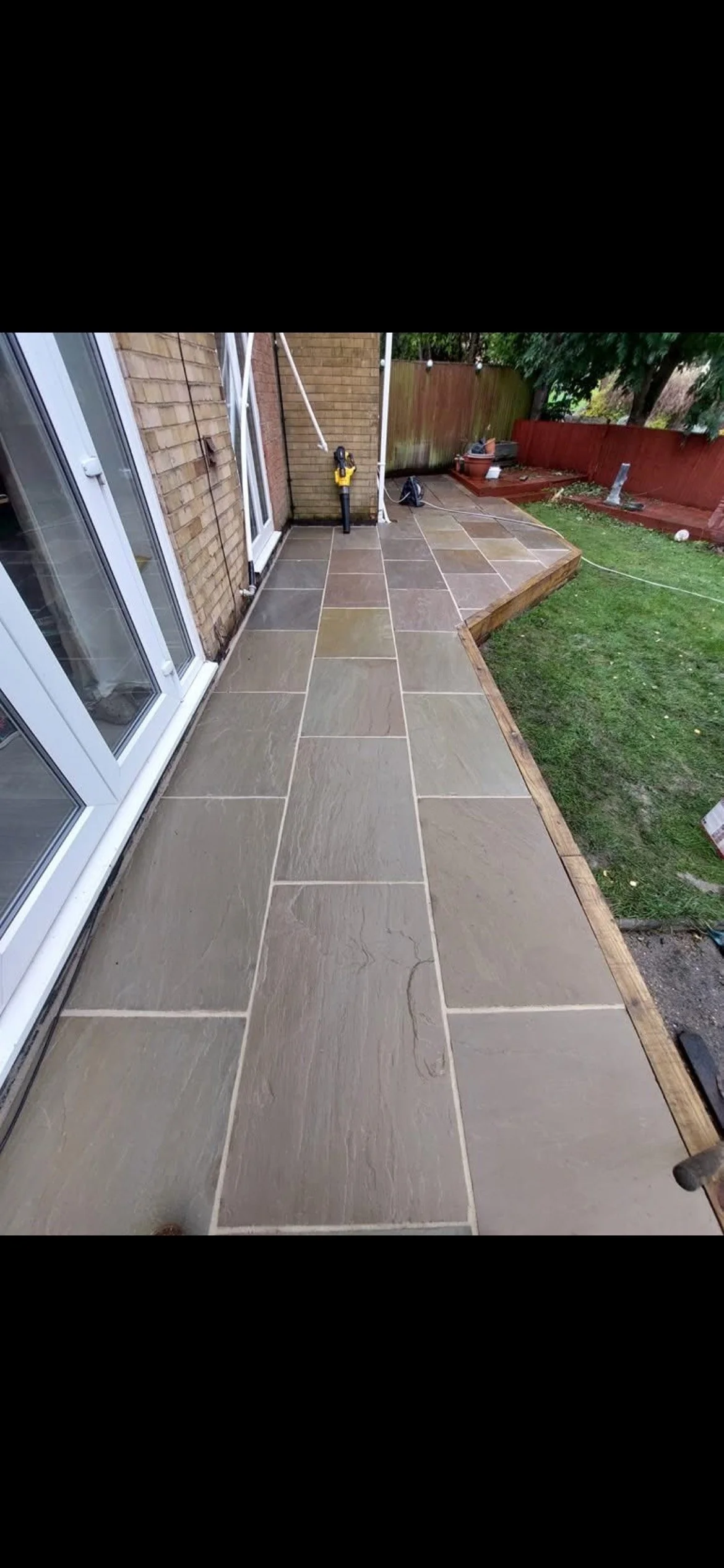 Newly installed stone patio with a border of wood planks in a backyard.