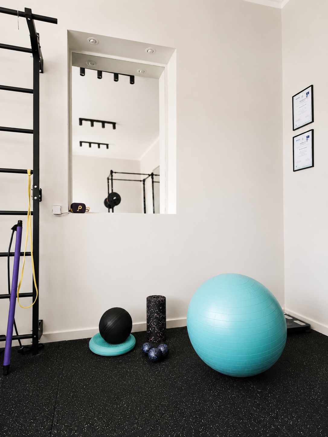 Home gym with black exercise equipment, stability ball, foam roller, and small weights on a speckled black floor.