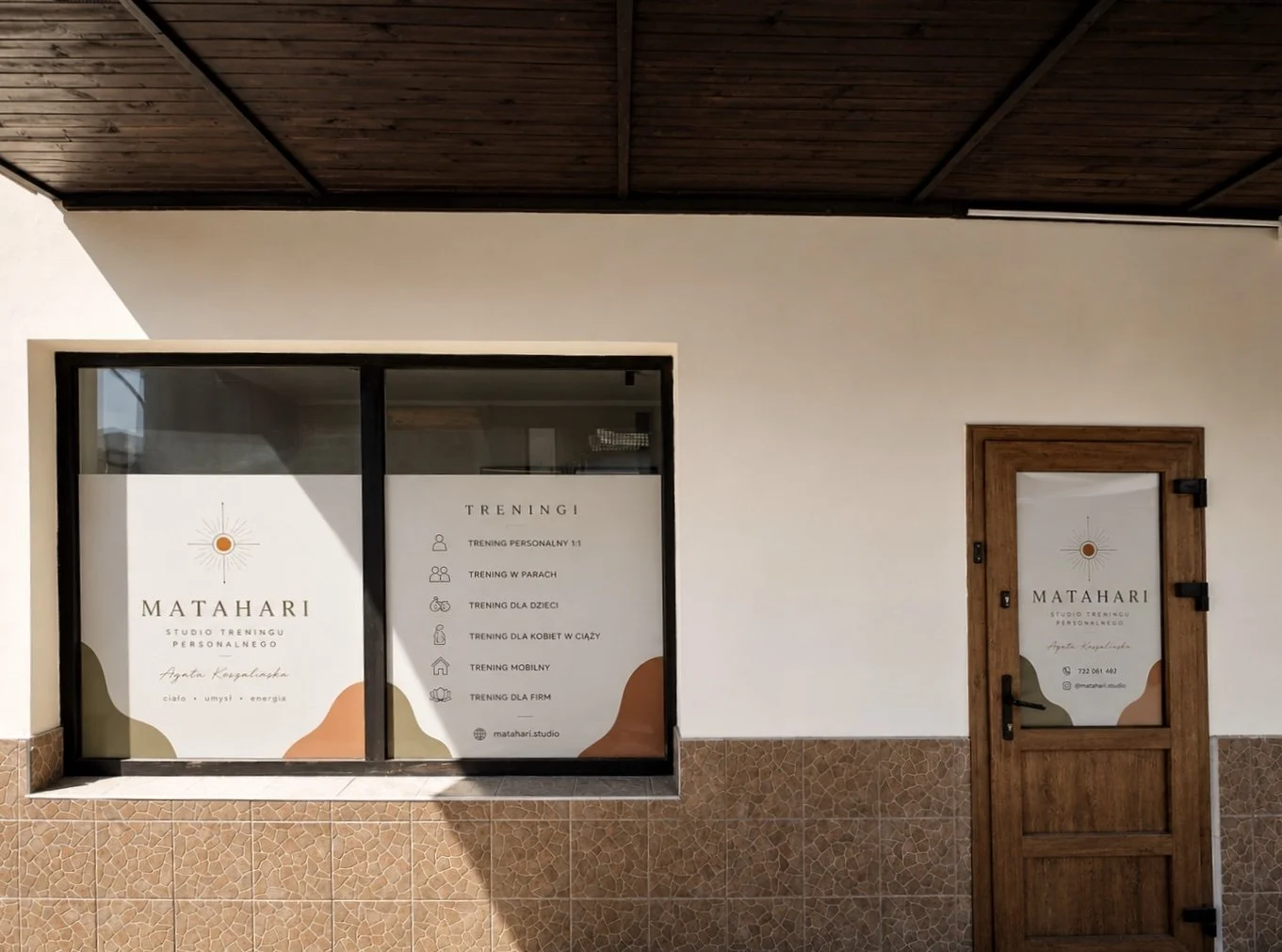Exterior view of a studio training business called Matahari, showing a window and a wooden door with signs listing training services and contact information.