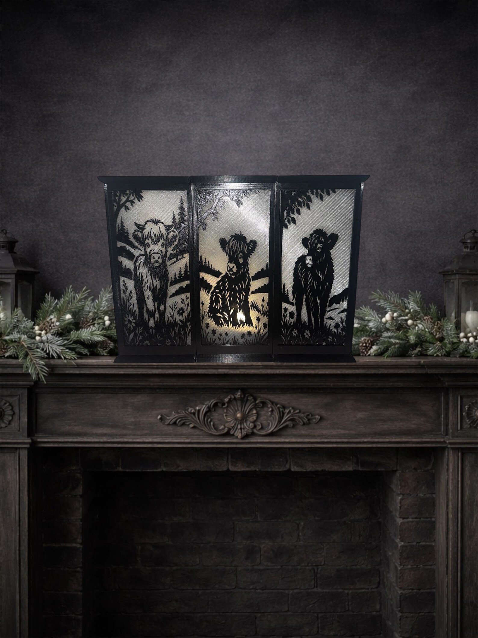 Decorative black metal candle lantern with cut-out design of three bears, placed on a fireplace mantel with greenery, in a dimly lit room.