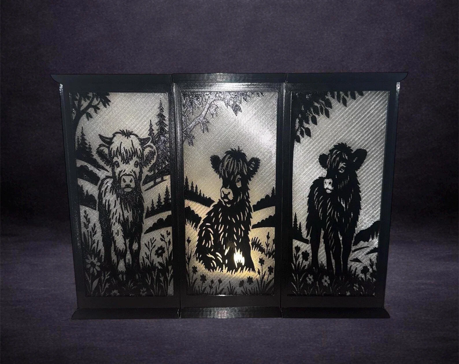 Decorative black metal lantern with cut-out images of three different calves in a forest setting, with a small candle inside.