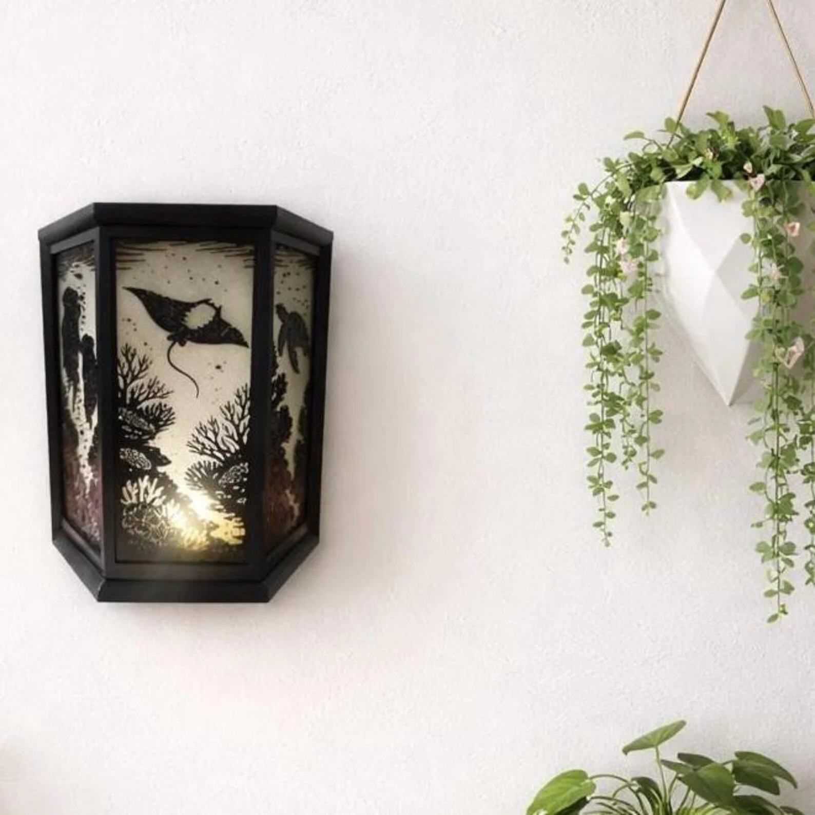 Decorative wall light with silhouette nature scene and hanging potted plant with trailing vines.