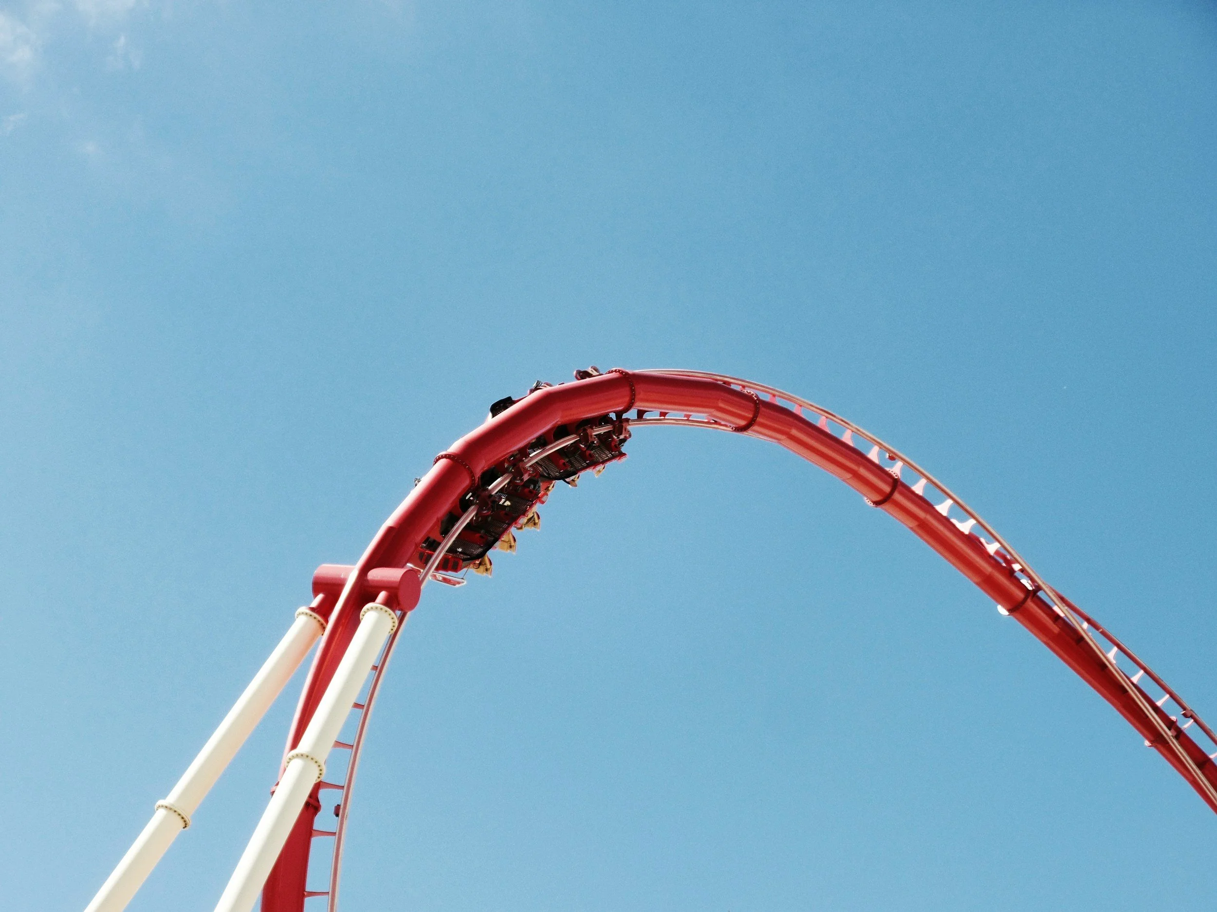 A red rollercoaster mid-inversion on a red track with white struts, against a bright blue sky