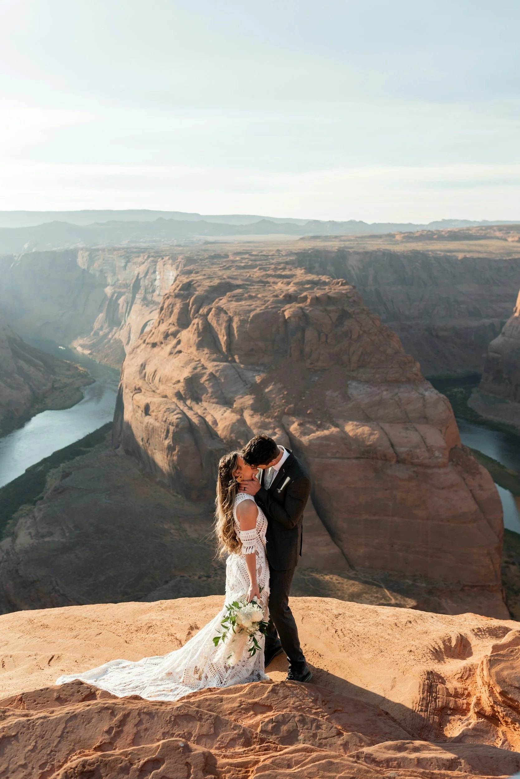 A bride and groom kissing atop a sunny outcrop in the Grand Canyon