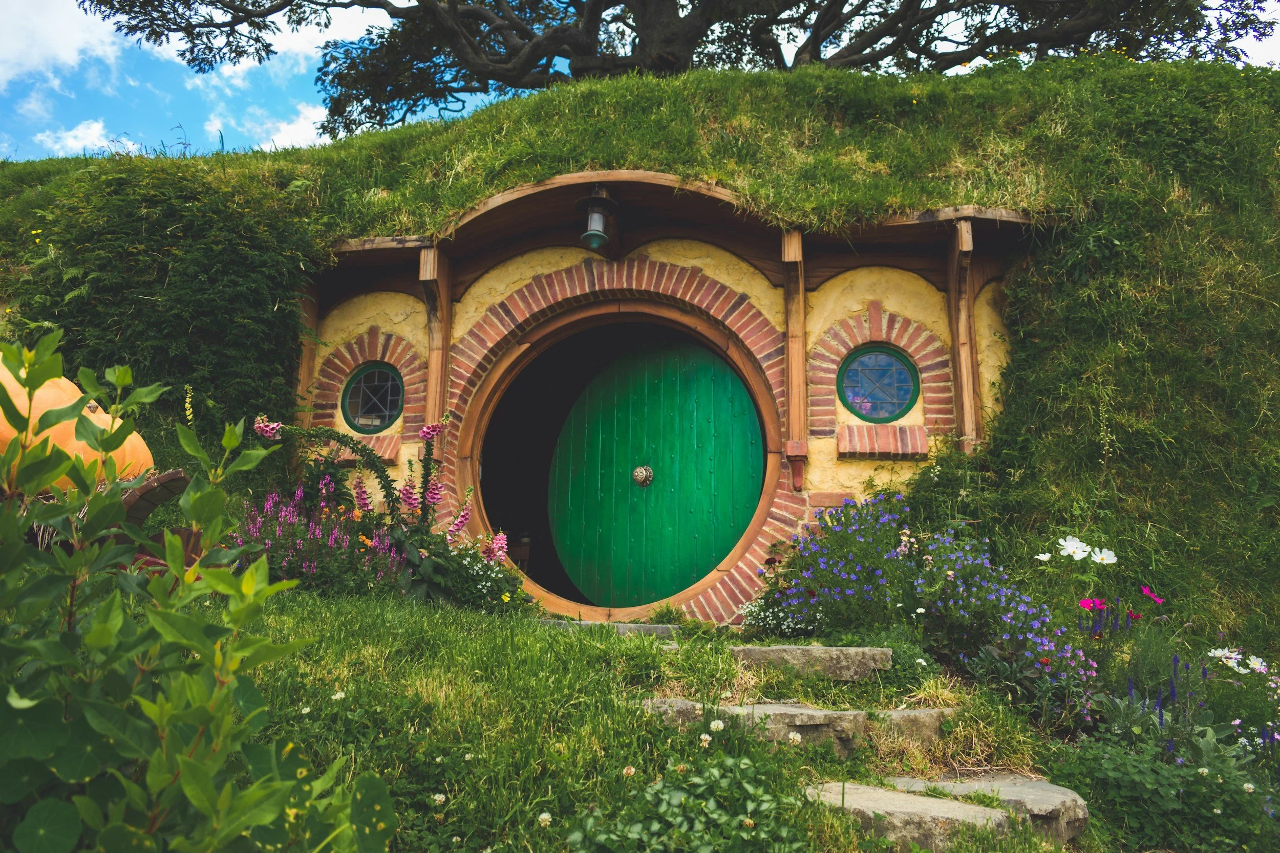 The round green front door of Bag End from the Lord of the Rings, Hobbition film set in Aotearoa New Zealand, partially open on a sunny day.