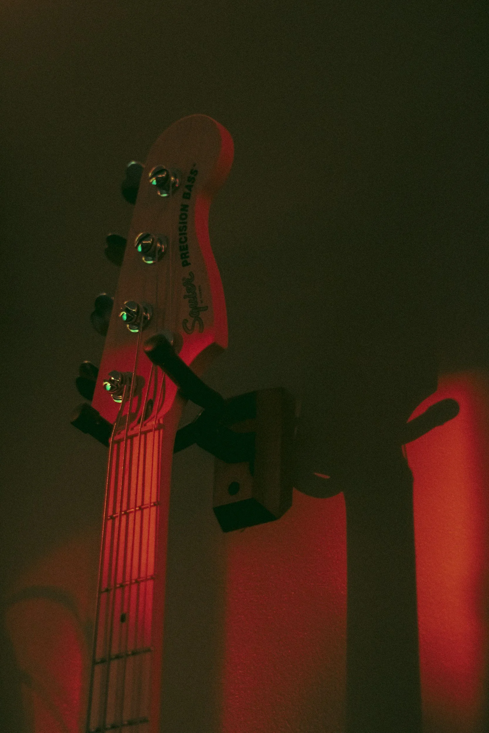 Bass headstock with tuning pegs and strings, illuminated by red lighting, with the words 'Squier' and 'Precision Bass' visible.
