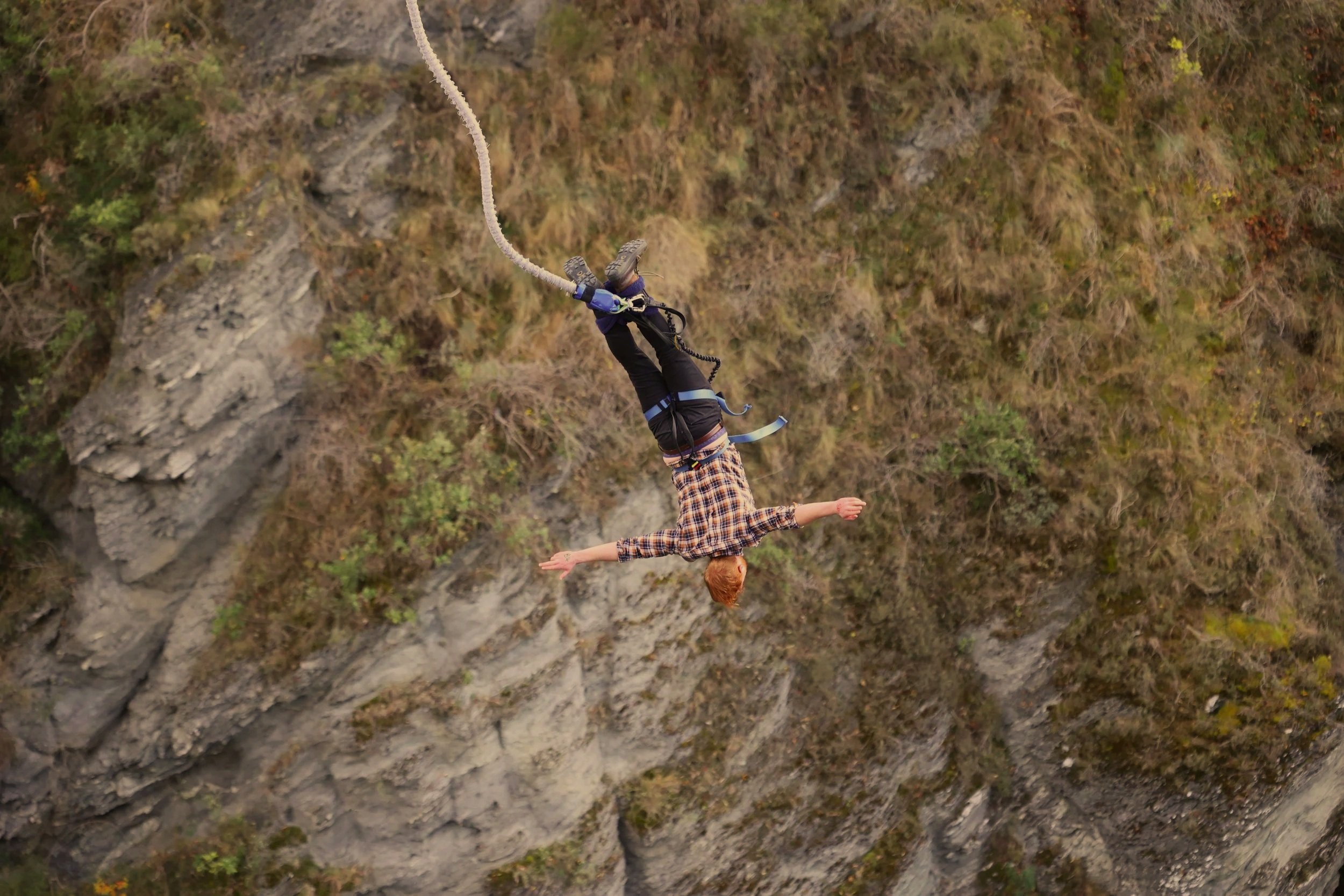 A person falling headfirst off a bungee cord above a rocky and wooded landscape.