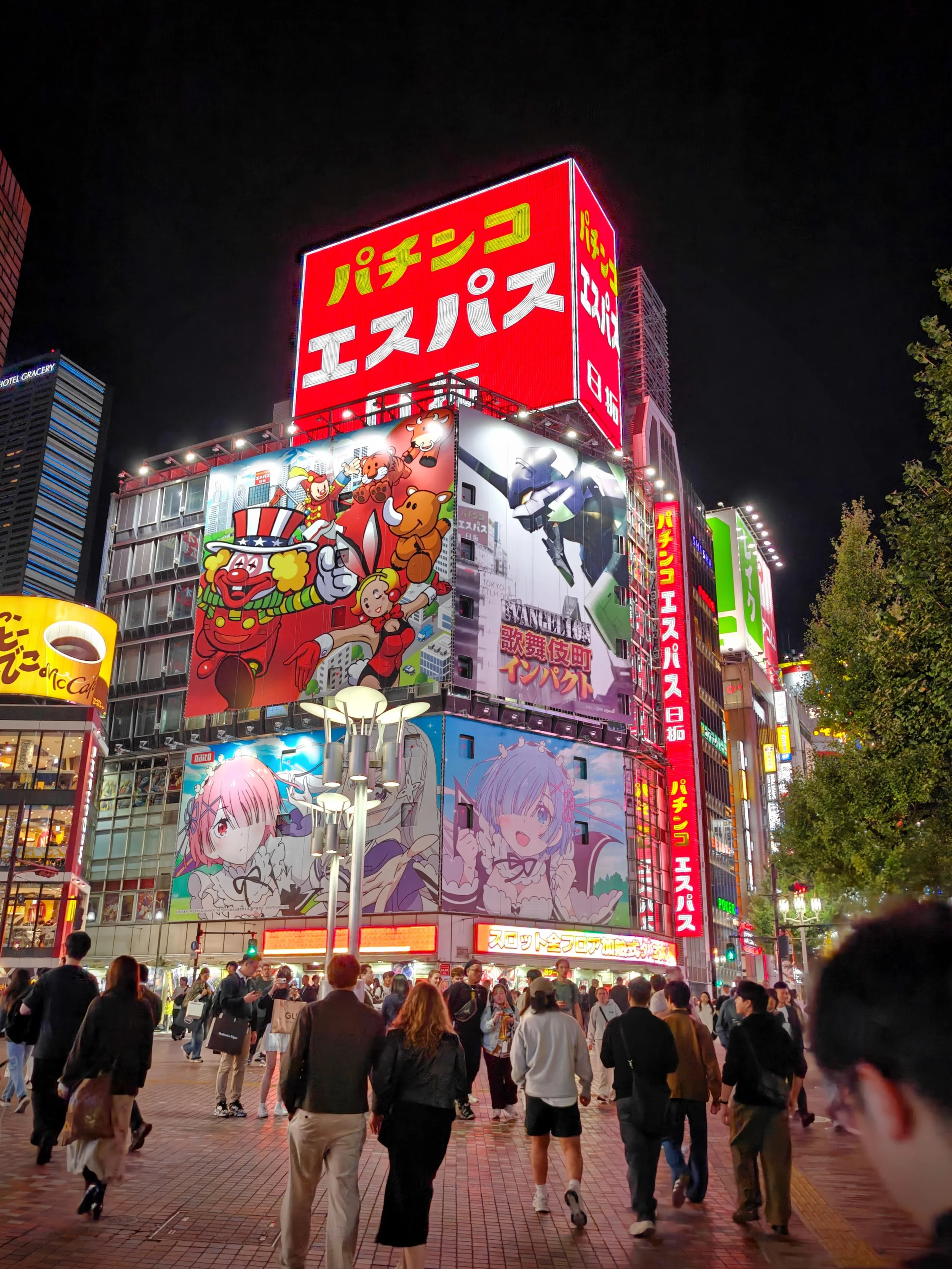 Bright neon billboards in a busy city at night, featuring colorful cartoon characters and Japanese signage, with pedestrians walking on the street.