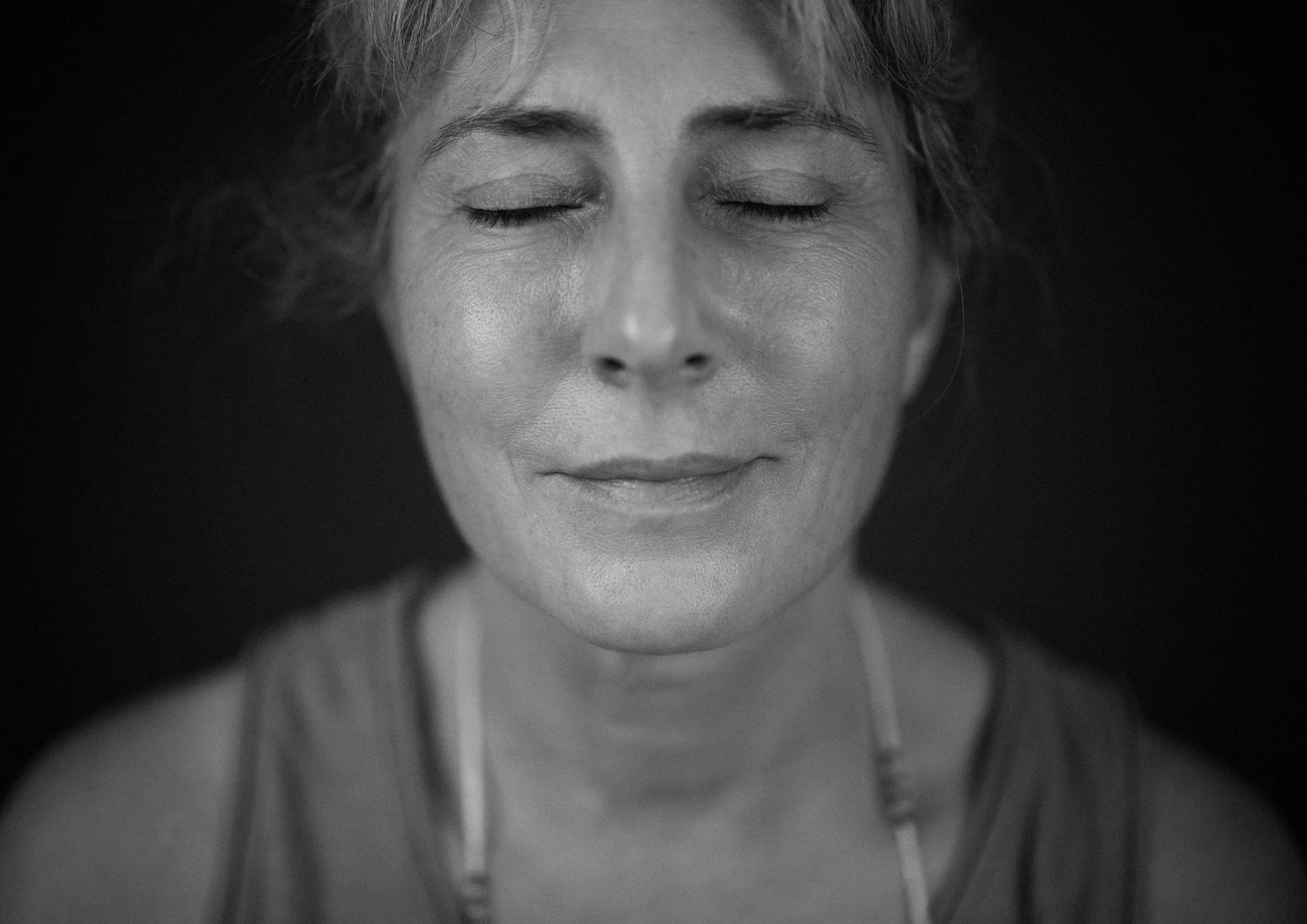 Black and white close-up portrait of a woman with her eyes closed, smiling gently.