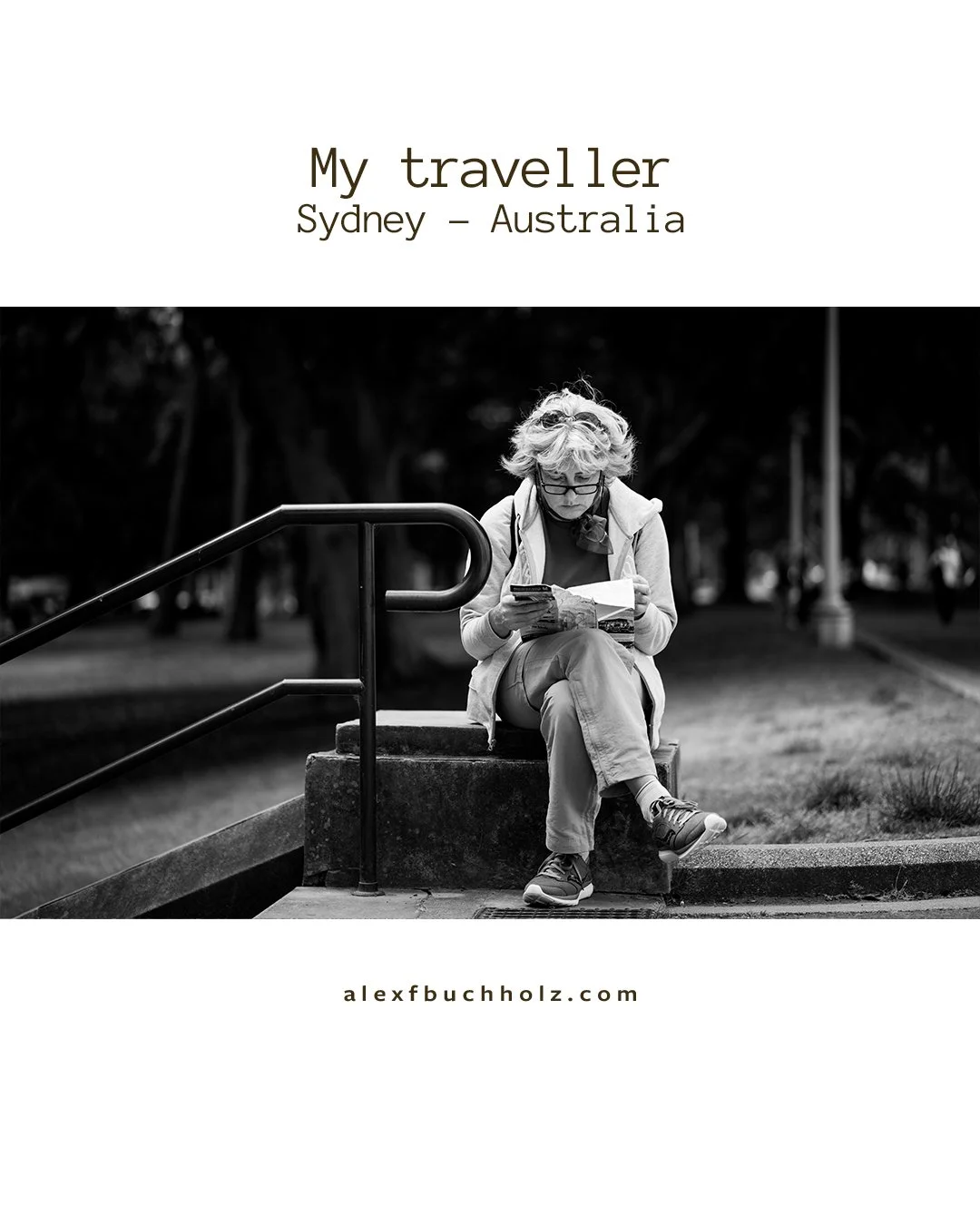 Black and white photo of a woman sitting on a concrete ledge reading a map or brochure, with a park in the background.