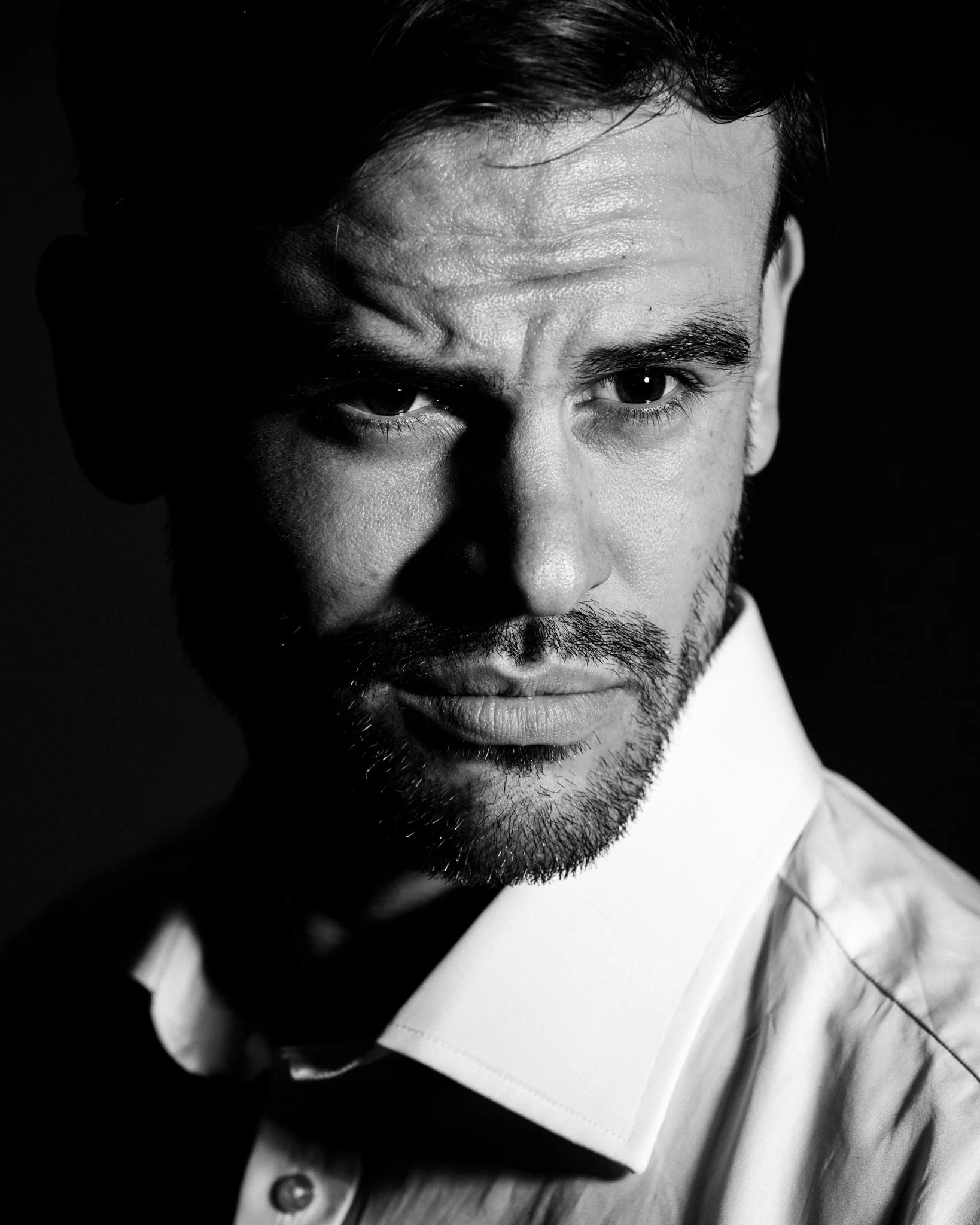 Close-up black-and-white portrait of a man with dark hair, beard, and mustache, wearing a white shirt and a bow tie.
