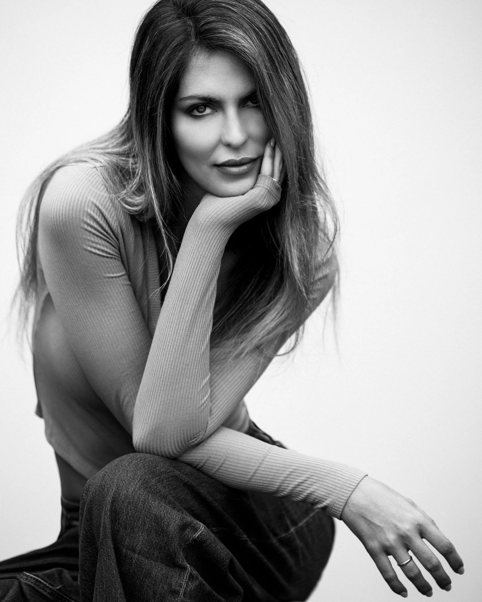 Black and white portrait of a woman with long hair, resting her chin on her hand, looking at the camera.