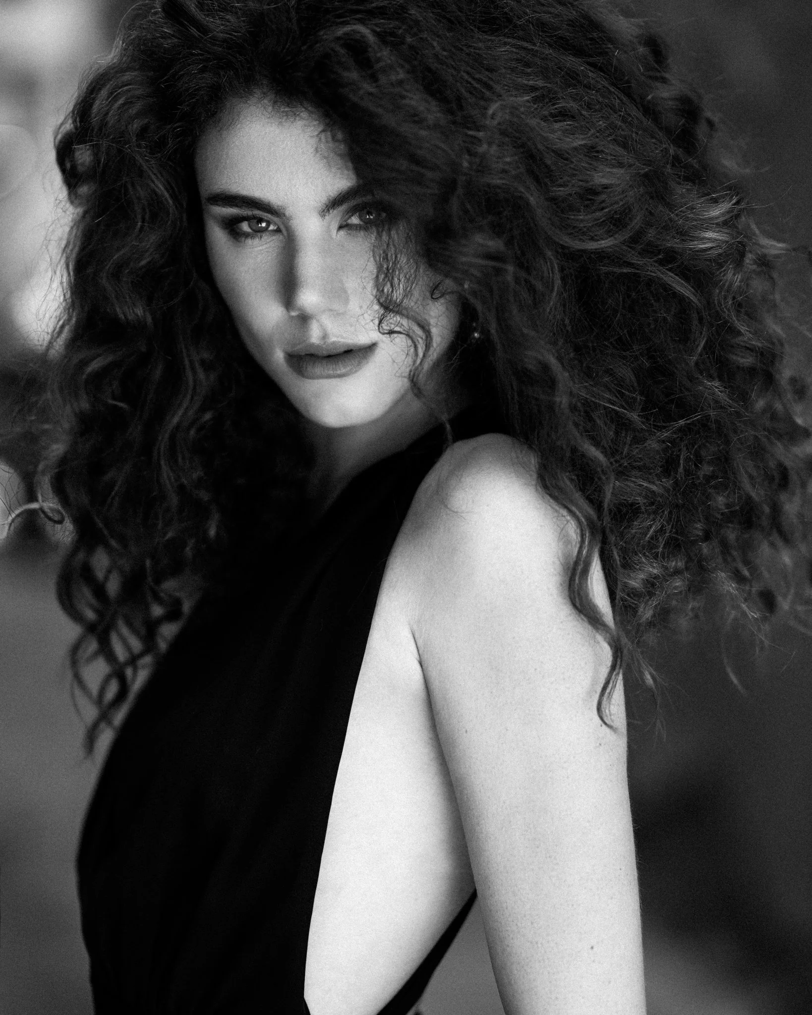 Black and white photo of a woman with dark, curly hair, looking at the camera with a serious expression, her face partially obscured by her hair.