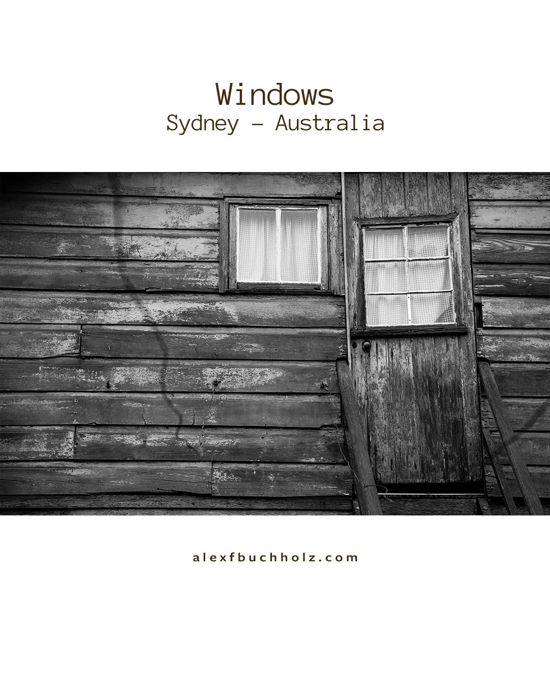 Black and white photo of a weathered wooden house exterior with two small windows, one with curtains and a door with a window, in Sydney, Australia.