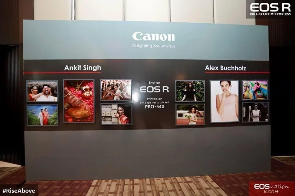 Display board showcasing photographs taken with the Canon EOS R camera, featuring two photographers named Ankit Singh and Alex Buchholz, with photo thumbnails of various scenes and people, and Canon branding at the top and EOS logo on the top right c