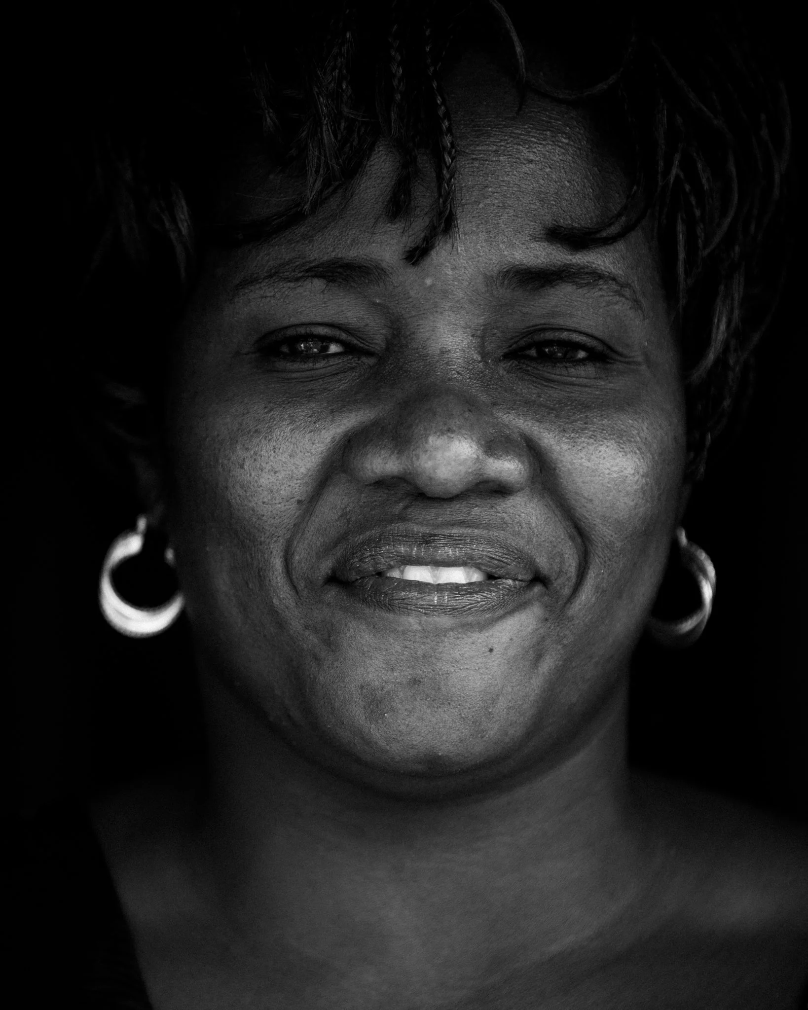 Black and white close-up portrait of a smiling woman wearing hoop earrings and with curly hair.
