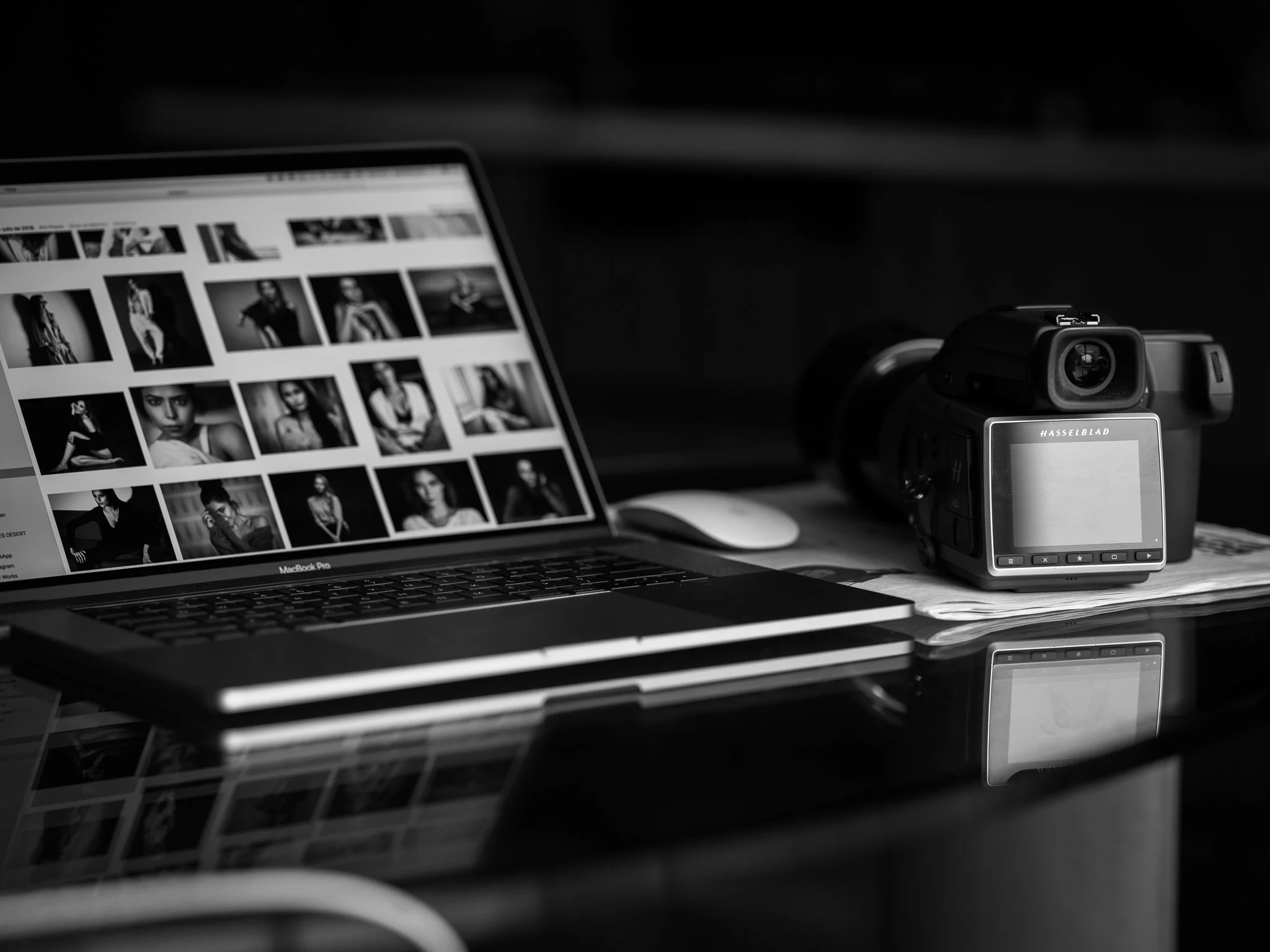A laptop displaying black and white photos of a woman in various poses, a desk scanner, and a mouse on a dark desk surface.