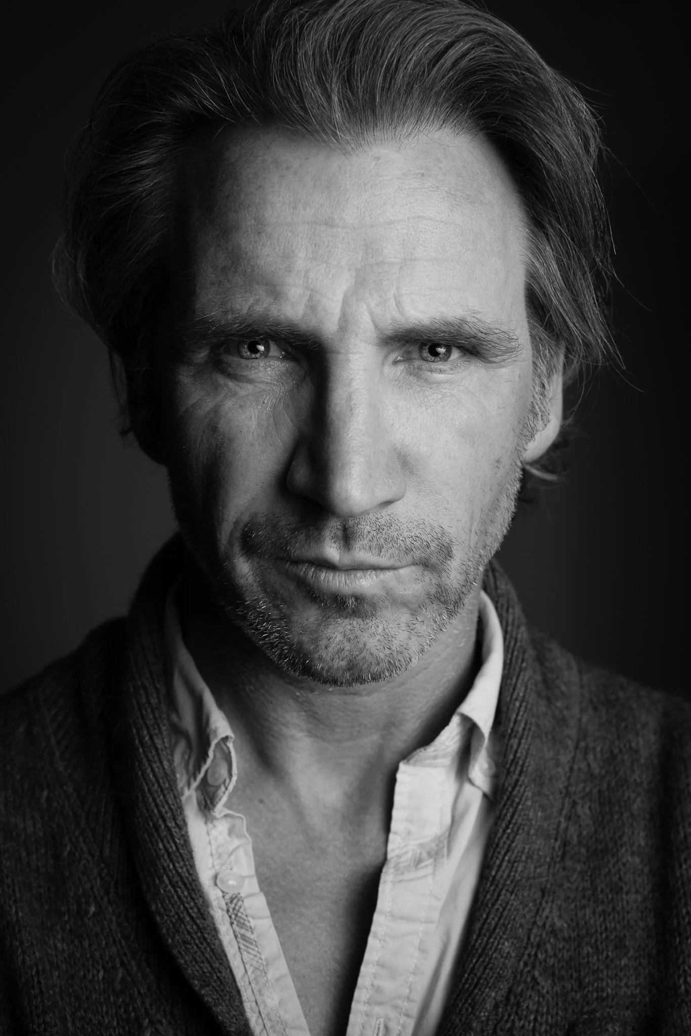 Black and white portrait of a middle-aged man with wavy hair, light eyes, and stubble, wearing a collared shirt and a cardigan.