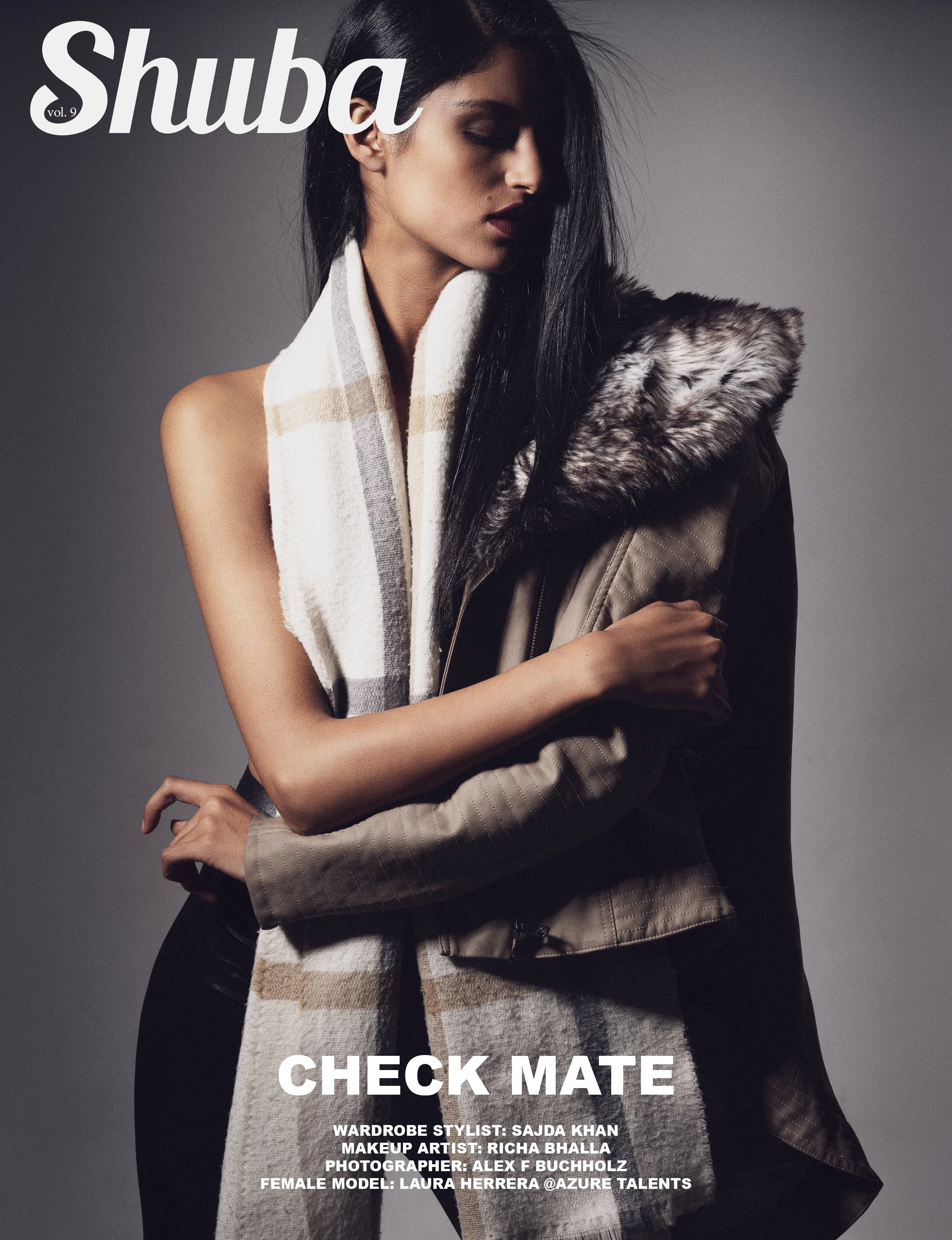 A fashion model with long dark hair, wearing a beige jacket with a fur-lined hood and a large striped scarf, poses against a neutral background.