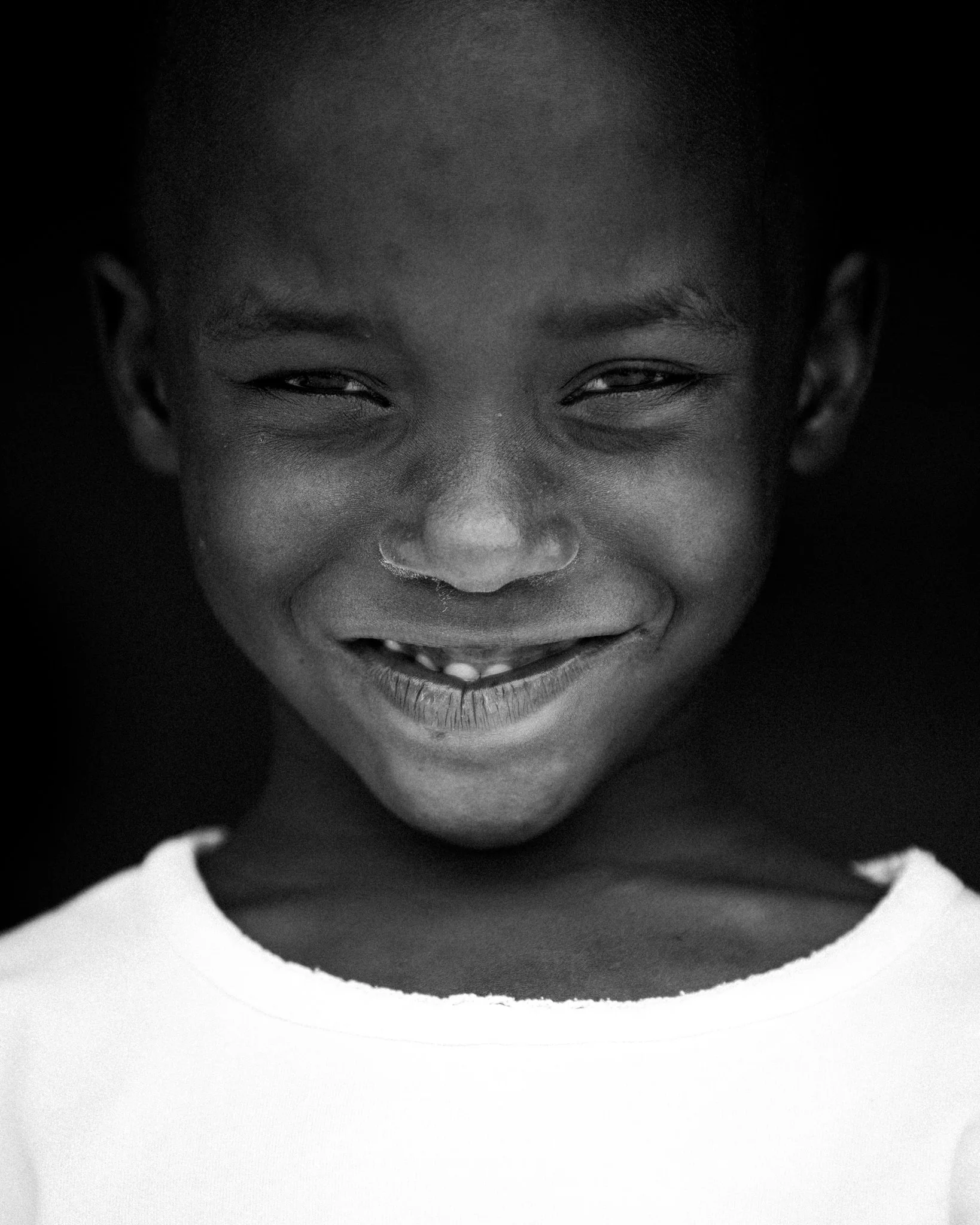 Black and white close-up of smiling young boy with short hair, wearing a white shirt.