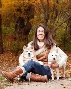 Woman poses in front of fall foliage with her two dogs
