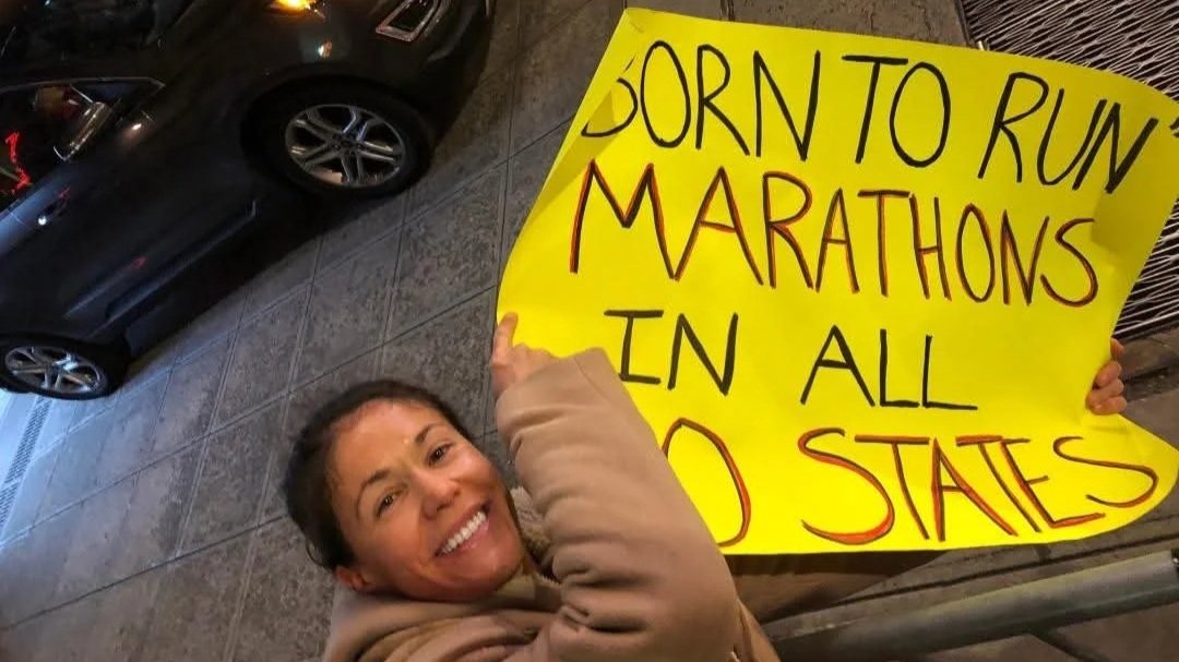 Woman holds sign that says Born to Run Marathons in All 50 States