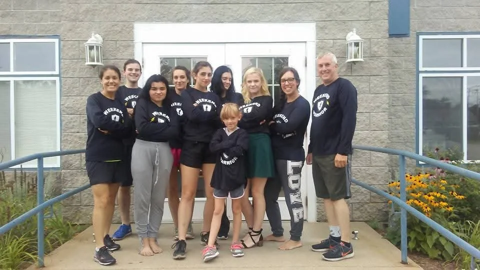 Group of 10 people standing in front of a building wearing running shirts that say Weekend Warrior