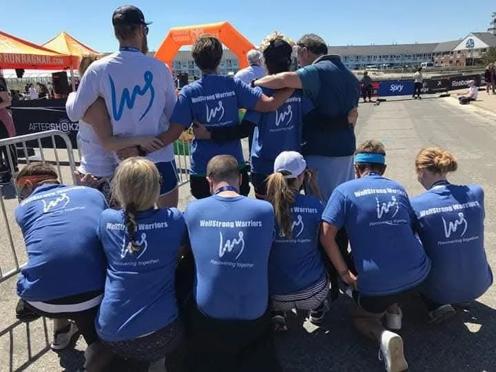 Group of people with their backs to the camera showing off the back of their WellStrong Warriors t-shirts