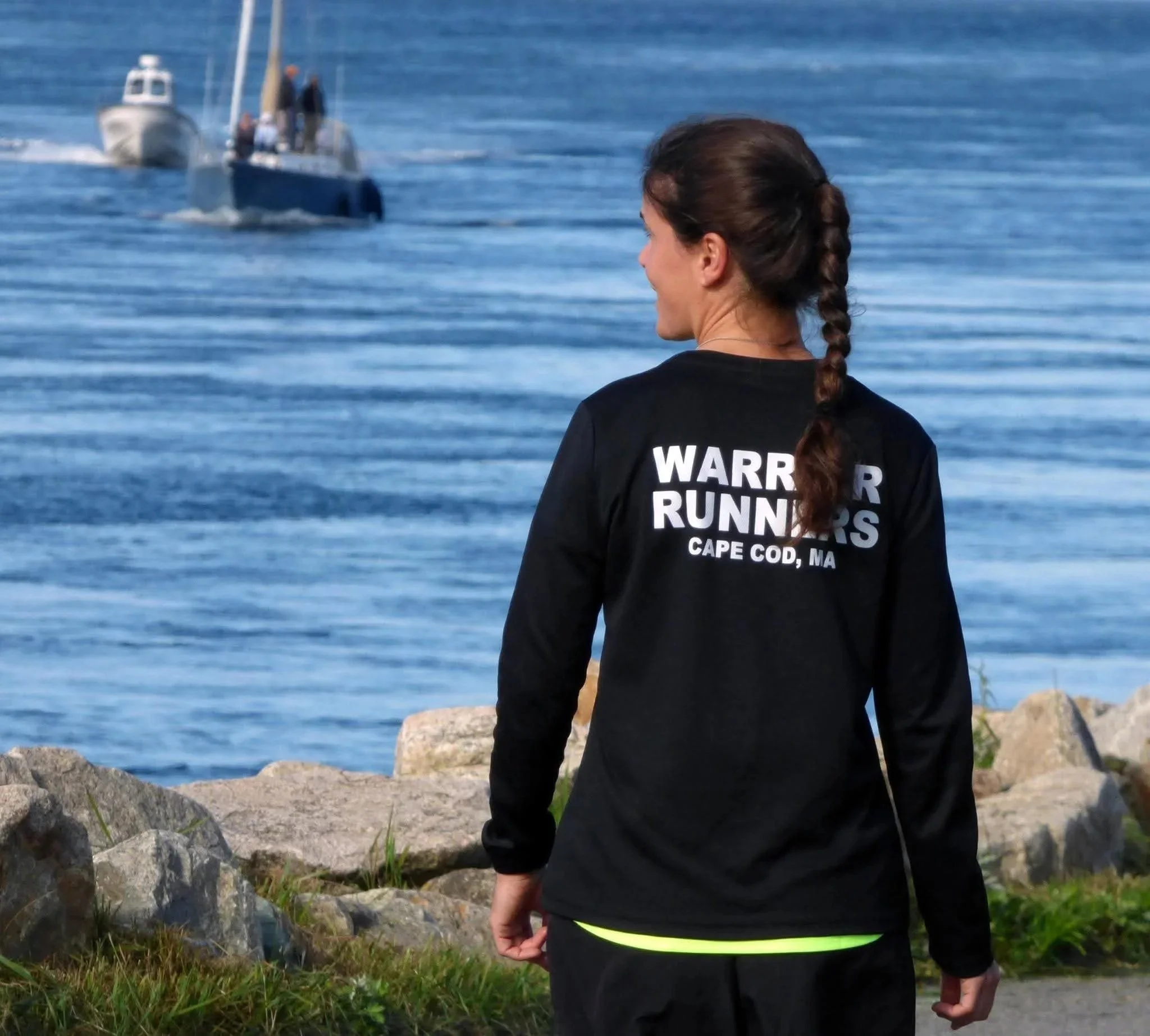 Image of a woman looking out over the water, wearing a black shirt that says Warrior Runners