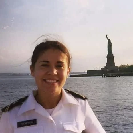 Woman in U.S. Navy dress white uniform poses with the Statue of Liberty in the background