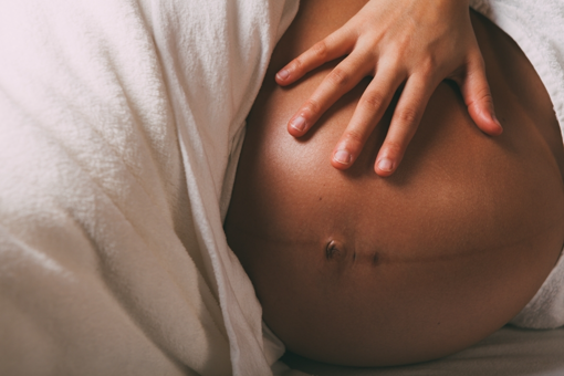 Une main repose sur un ventre de femme enceinte illustrant un acte de massage prénatal.