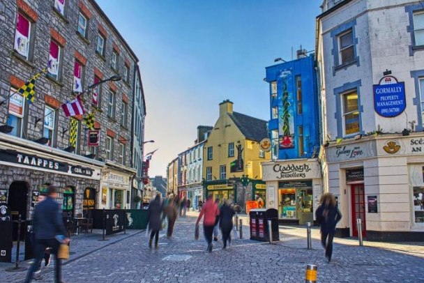 People walking on a cobblestone street surrounded by colorful buildings and shops in a city.