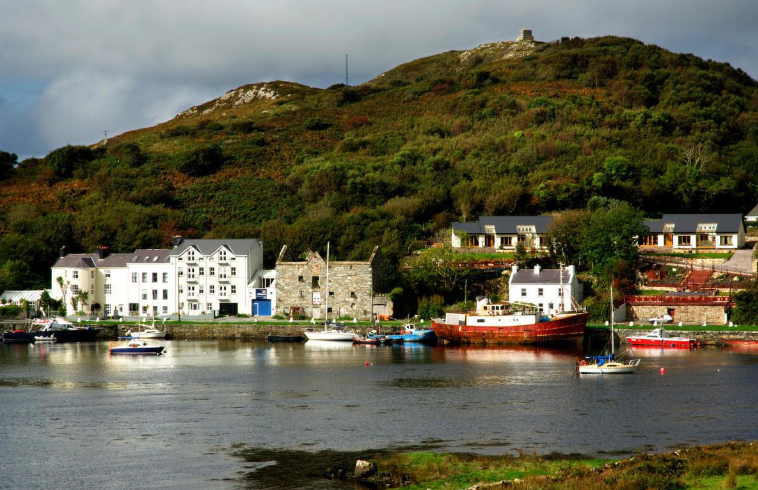 A waterfront scene with white buildings, boats, and a hillside in the background.