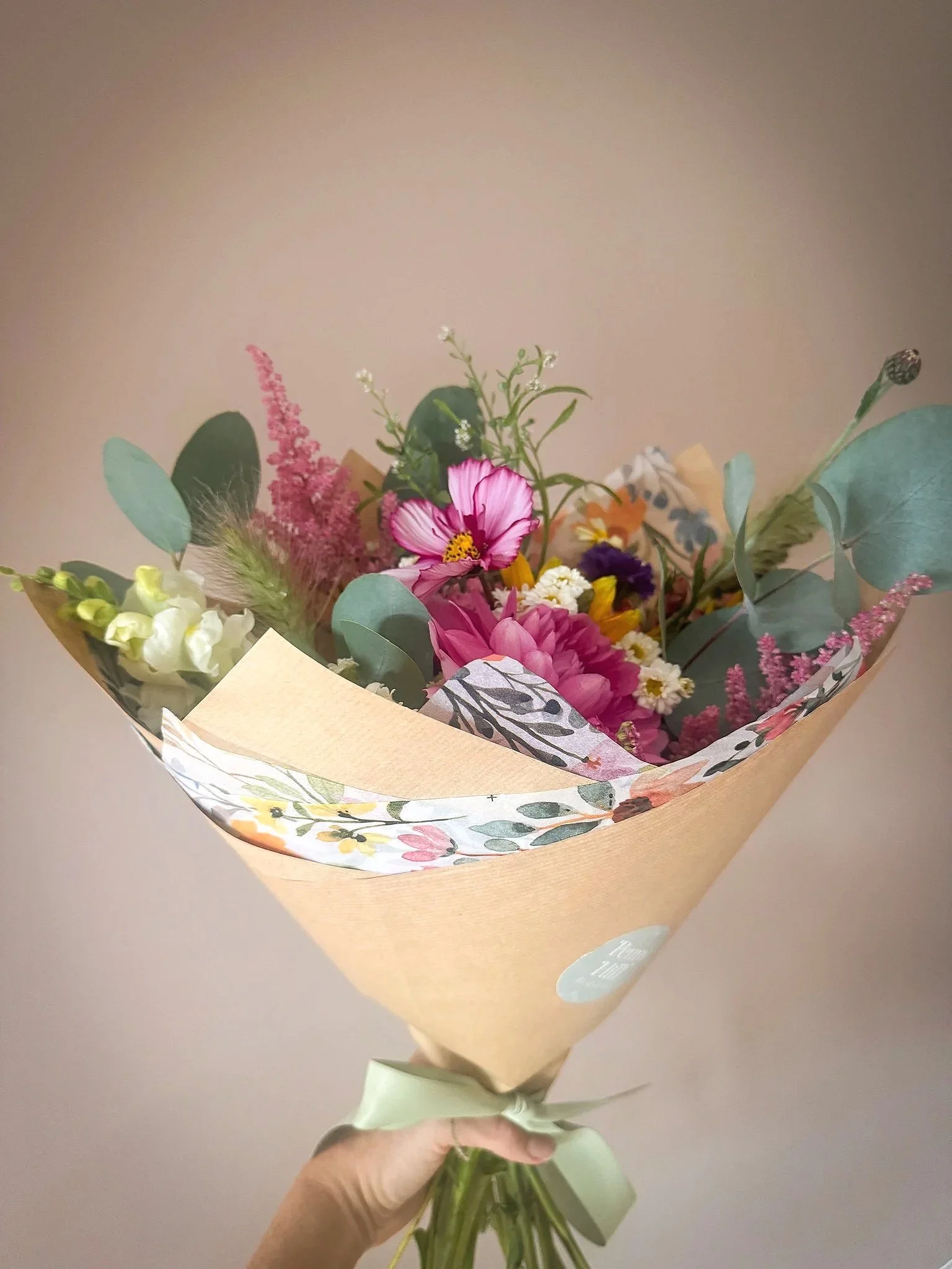 Colorful bouquet of fresh flowers wrapped in decorated paper, held by a hand with a ribbon.