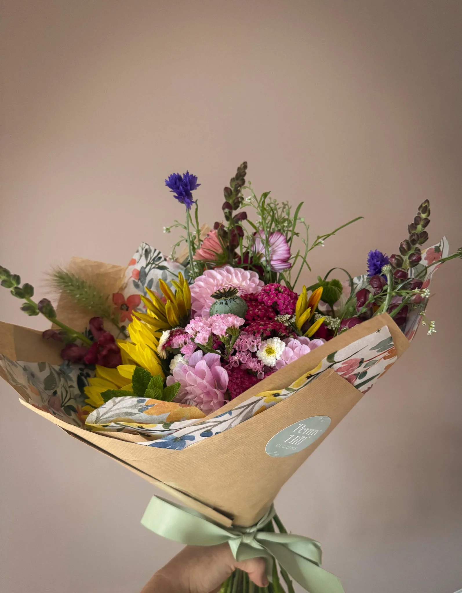 A colorful bouquet of flowers including pink, yellow, purple, and white blossoms wrapped in decorative paper with a green ribbon.