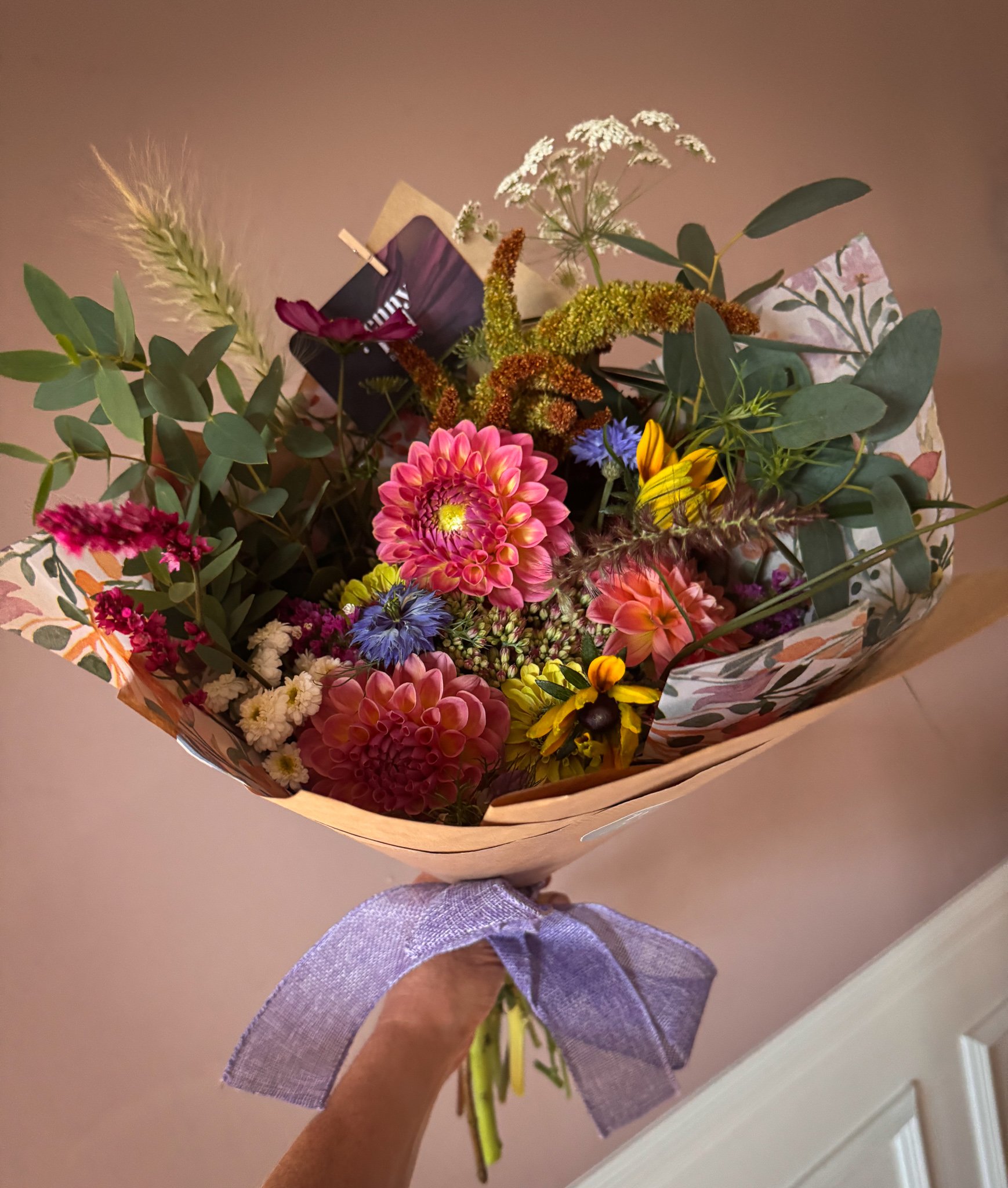 Colorful bouquet of flowers with pink, purple, yellow, and white blooms, wrapped in decorative paper with a purple ribbon.