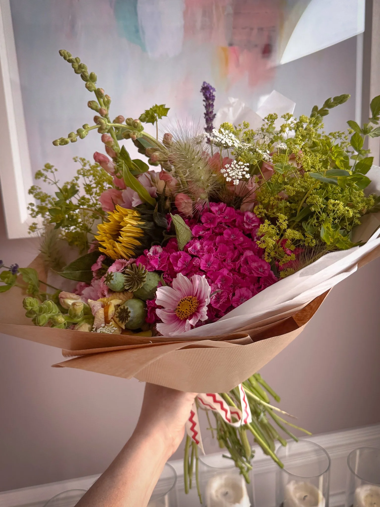 Hand holding a colorful bouquet of various flowers wrapped in brown and white paper